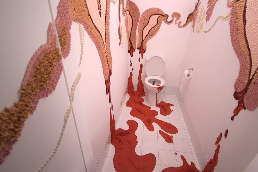 A large colourful image of a menstruating uterus bleeding onto the floor on the walls of a toilet cubicle.