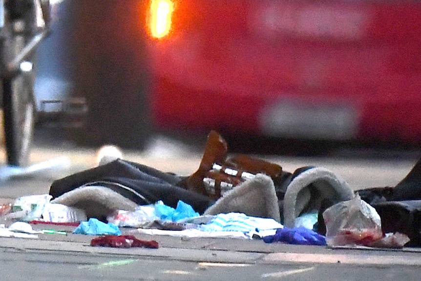 A close up of scattered cloth and items on pavement with police car lights blurred in background.