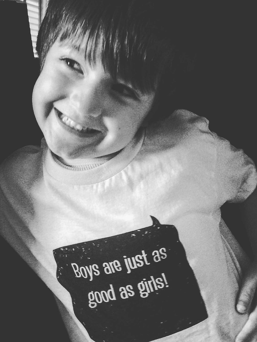 A boy smiles at the camera wearing a captioned T-shirt