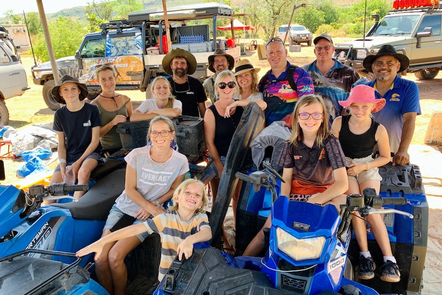 A group of people including adults and children, smiling, with some sitting on quad bikes.