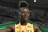 A Jamaican female sprinter poses for photographers with her gold medal and national flag.