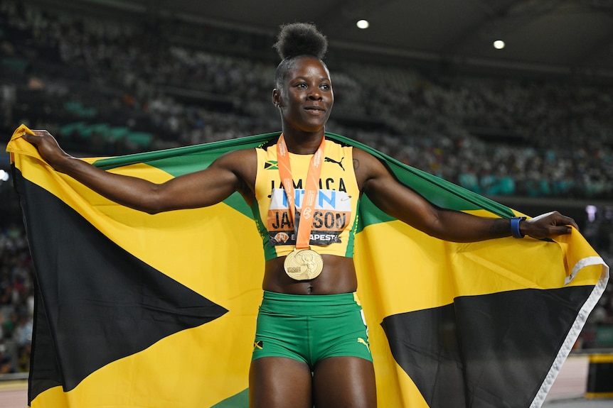 A Jamaican female sprinter poses for photographers with her gold medal and national flag.