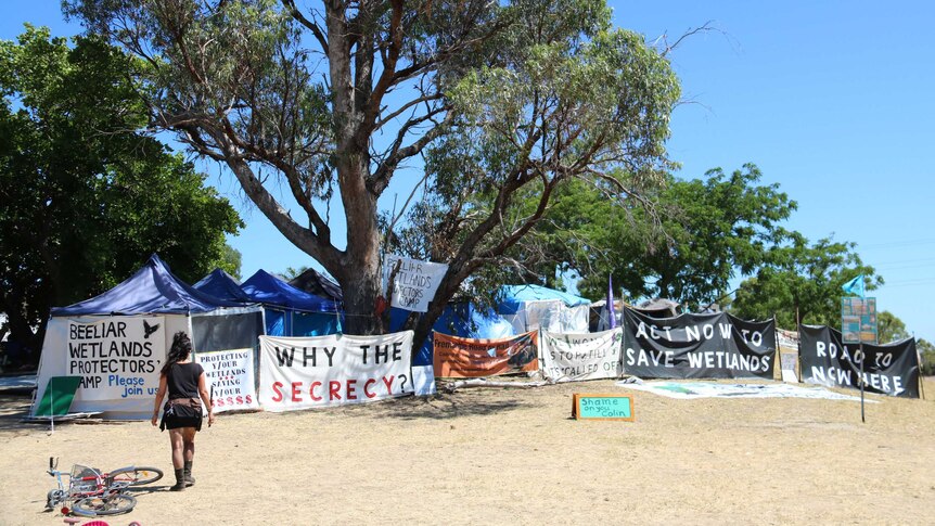 A protest camp outdoors with banners and tents under a large tree.