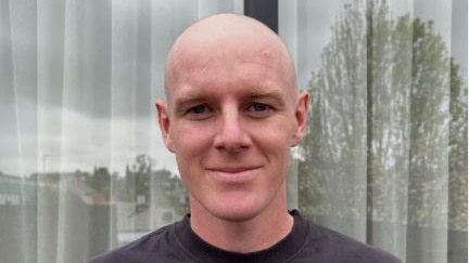 Man with a shaved head smiling for a photo 