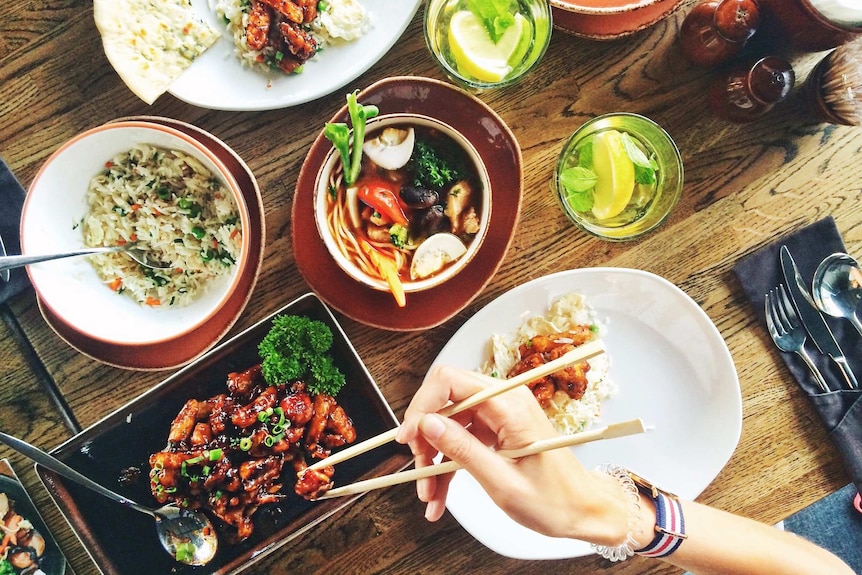 Top down photo of various Asian side dishes and plates, representing the idealised image of a family dinner.