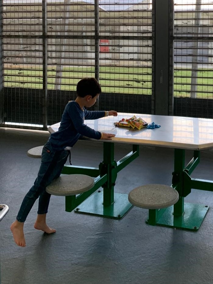 A boy in pyjamas leans over a table to select a treat with large fencing looming around him.