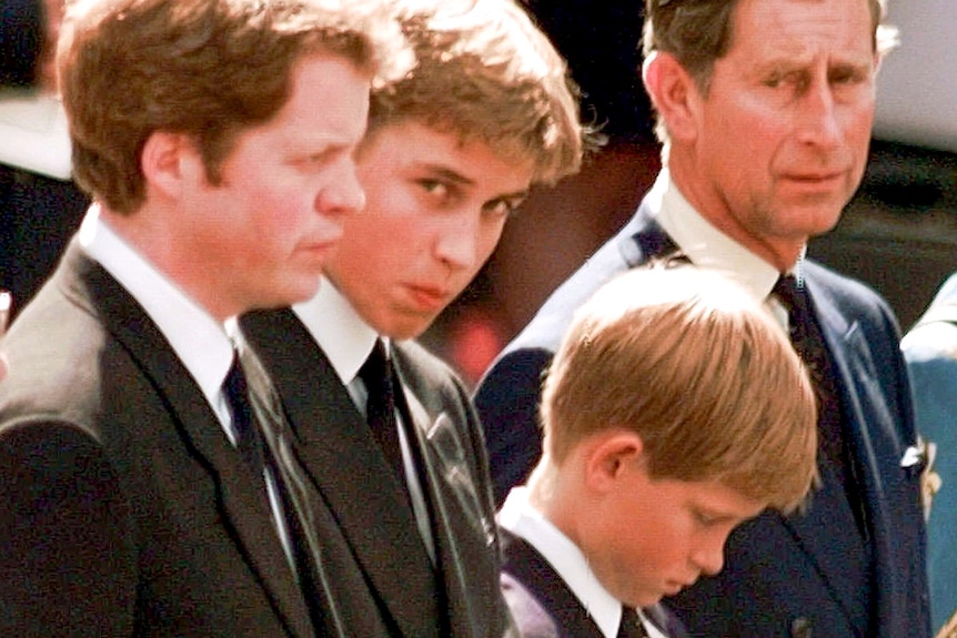 A small Prince Harry with his head bowed while William looks at the camera 