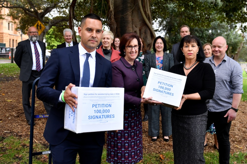 A man and a woman stand in front of a group, each holding a white box.