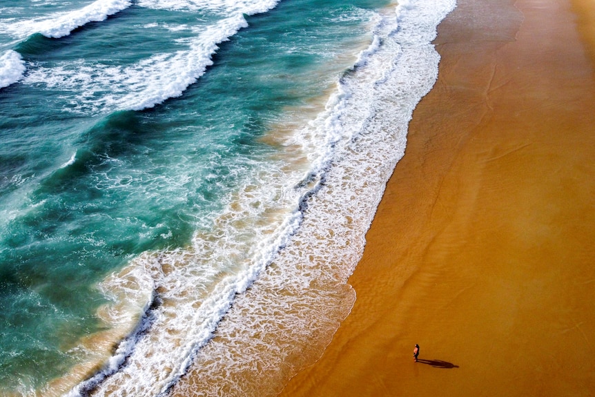 A drone shot of a man walking along an empty beach