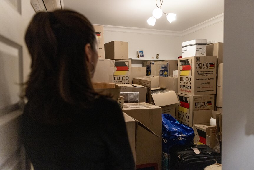 A woman gazes into a room stacked high with moving boxes. 