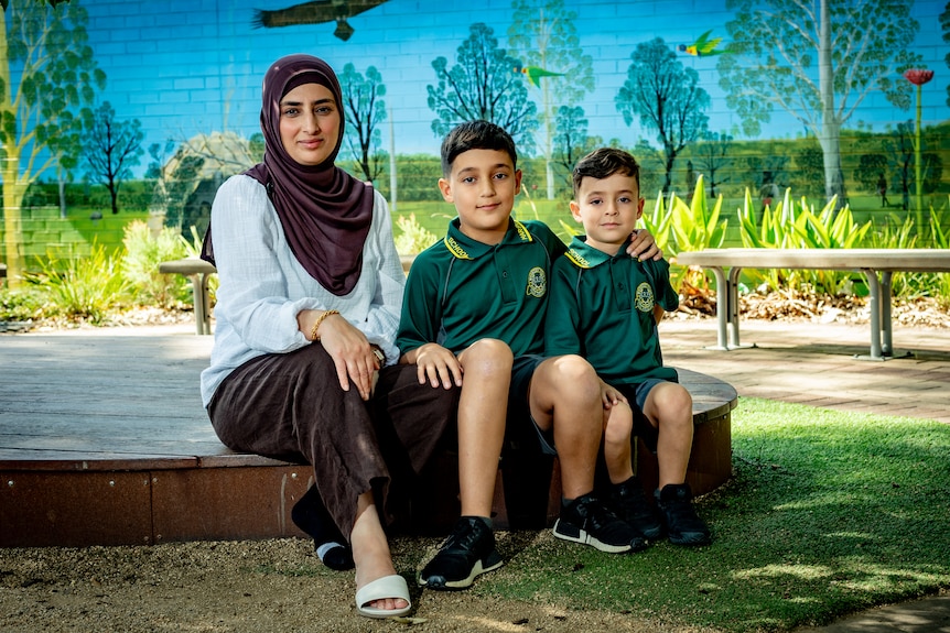 Ashty, wearing a hijab, sits next to her two young sons in a green school uniform.