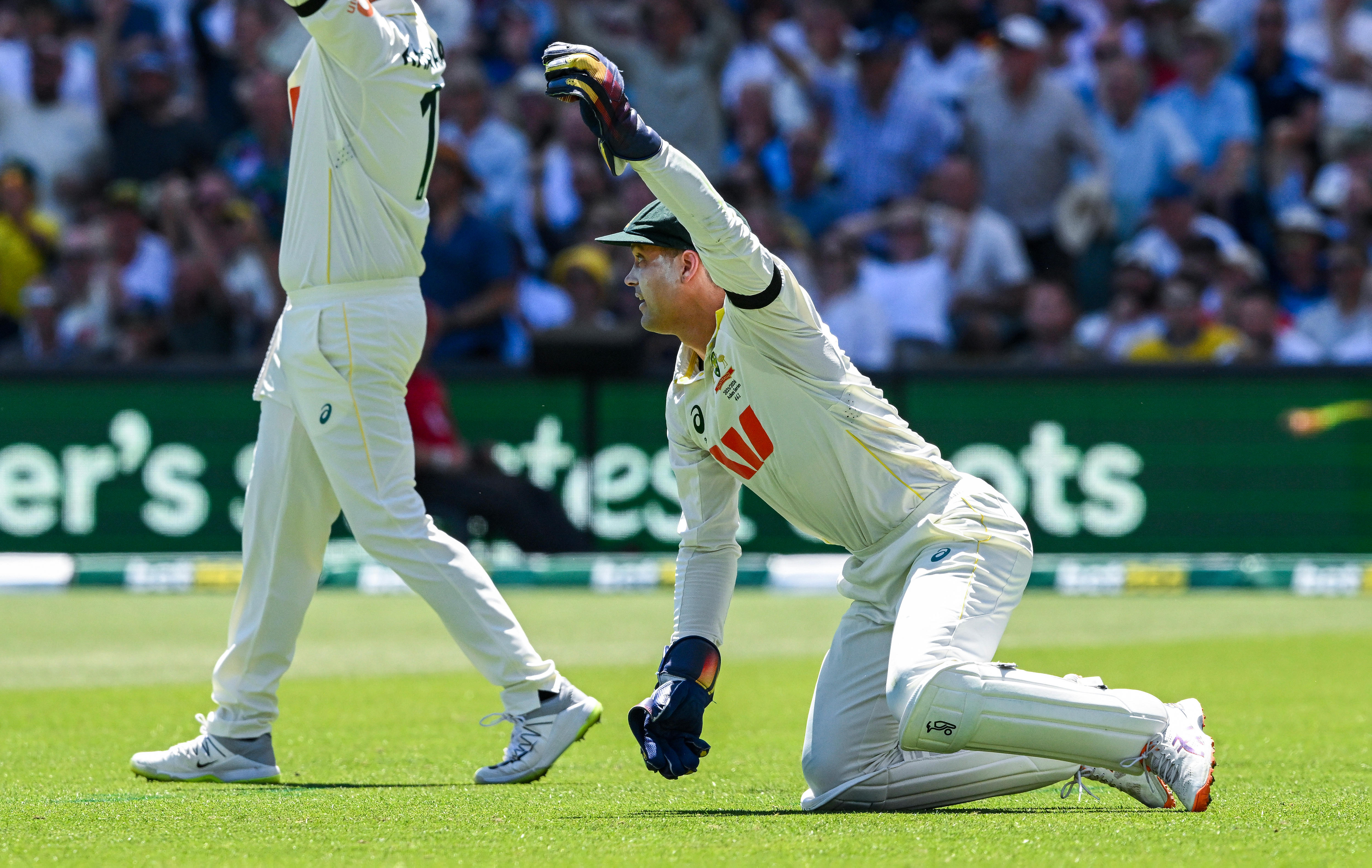 El portero australiano Alex Carey sostiene el balón con una mano sobre las rodillas durante una prueba.