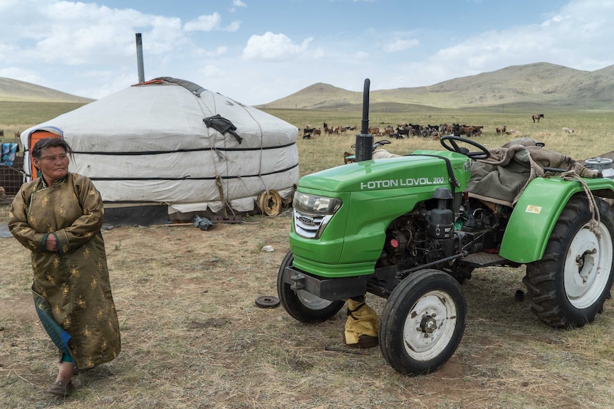 A woman stands beside a tractor outside her home in Mongolia.