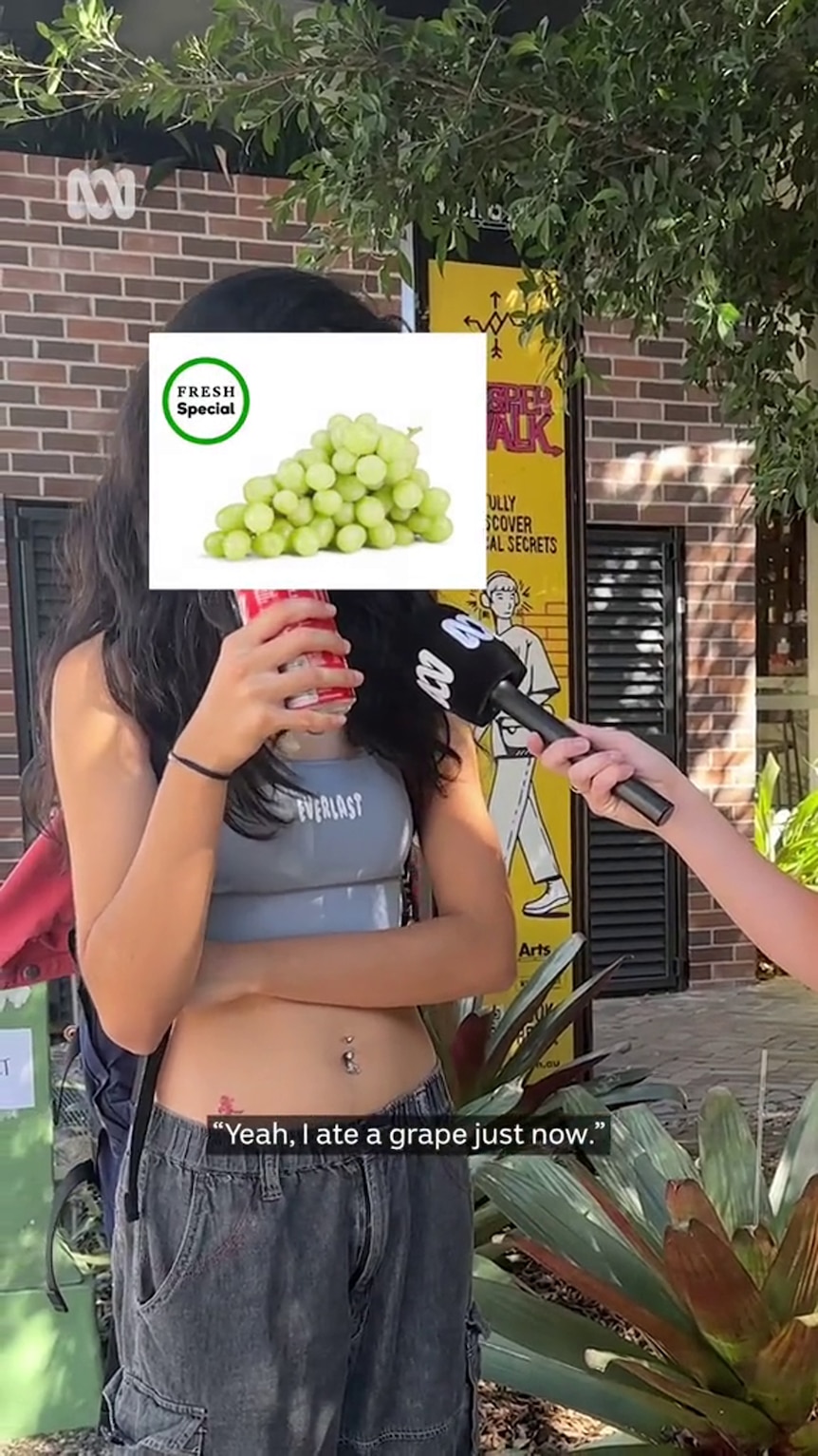A young woman  in street clothes is being interviewed and she has her face concealed with a graphic showing a bunch of grapes