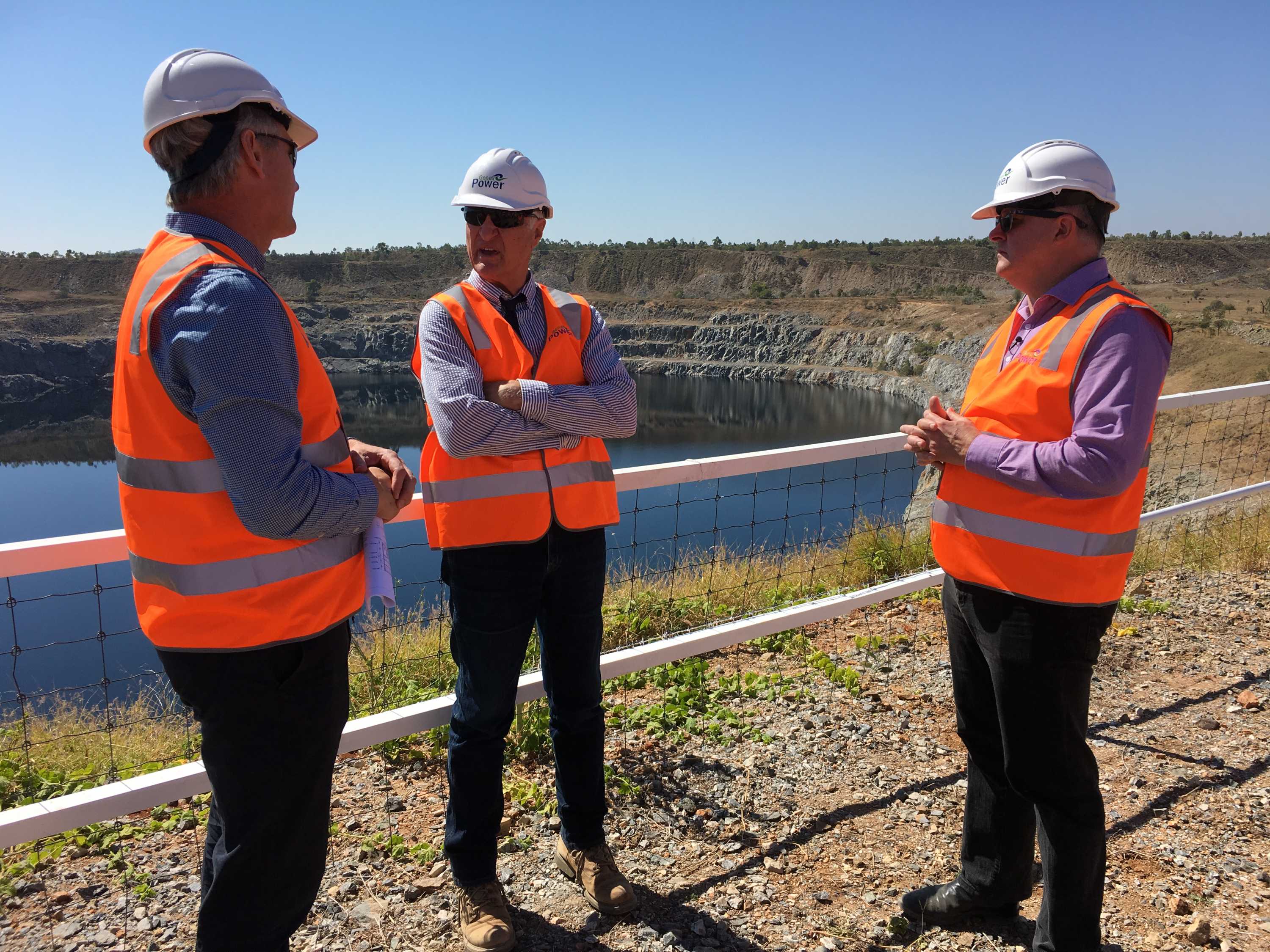Wearing high-vis vests and hardhats, Anthony Albanese and Bob Katter speak with Simon Kidston in front of a dam.