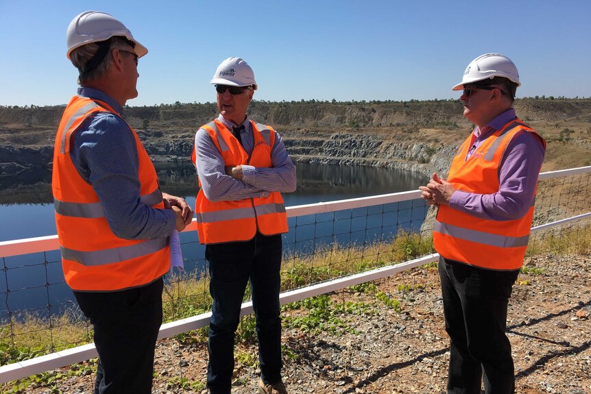 Wearing high-vis vests and hardhats, Anthony Albanese and Bob Katter speak with Simon Kidston in front of a dam.