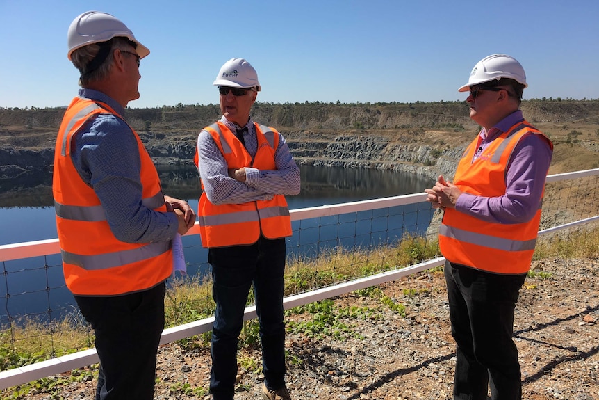 Wearing high-vis vests and hardhats, Anthony Albanese and Bob Katter speak with Simon Kidston in front of a dam.