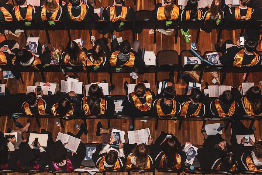 An overhead view of rows of graduating students seated with colorful scarves over their black academic robes.