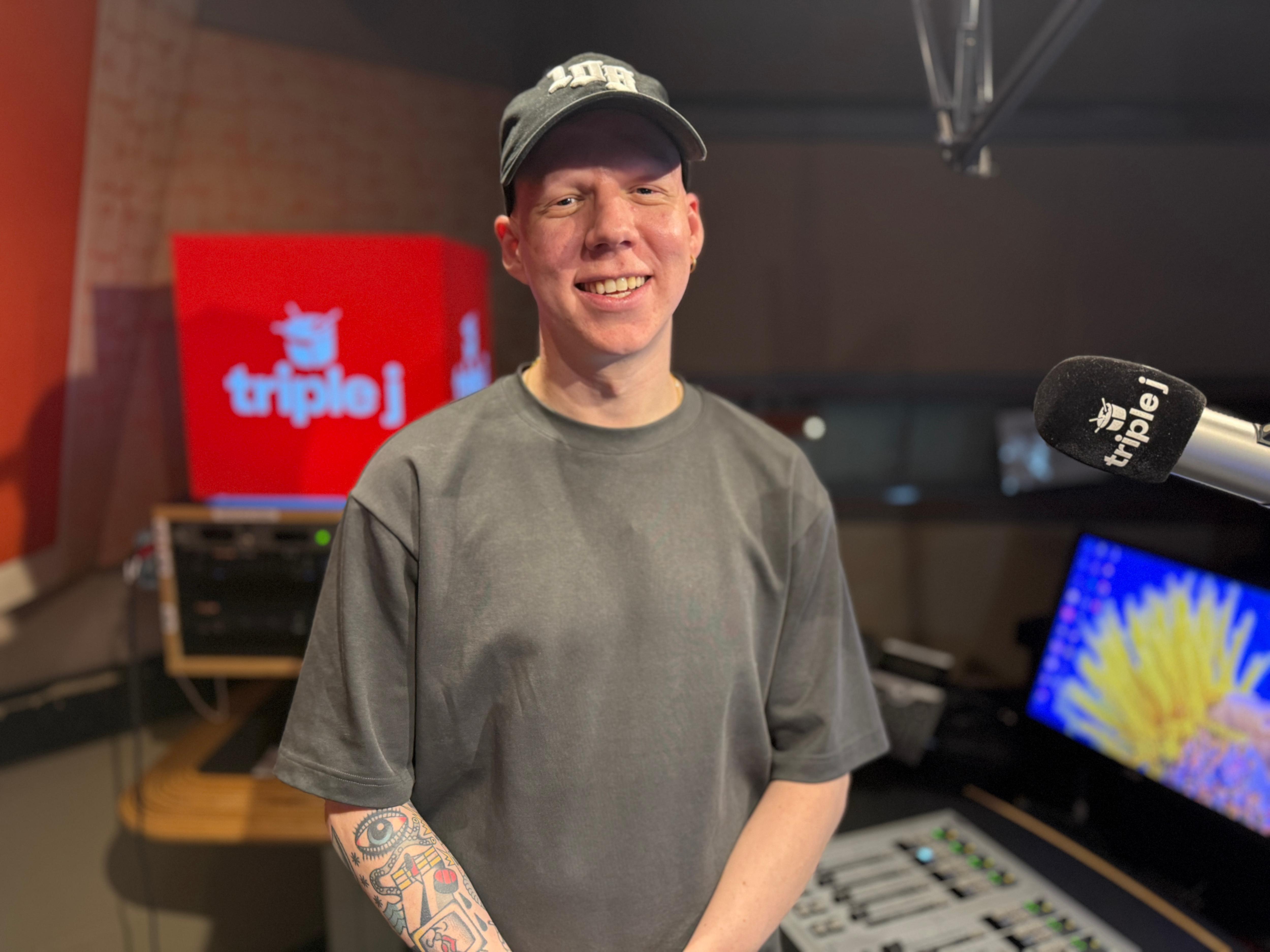 Um homem de camisa preta e boné está sorrindo ao lado de um microfone triplo J. 