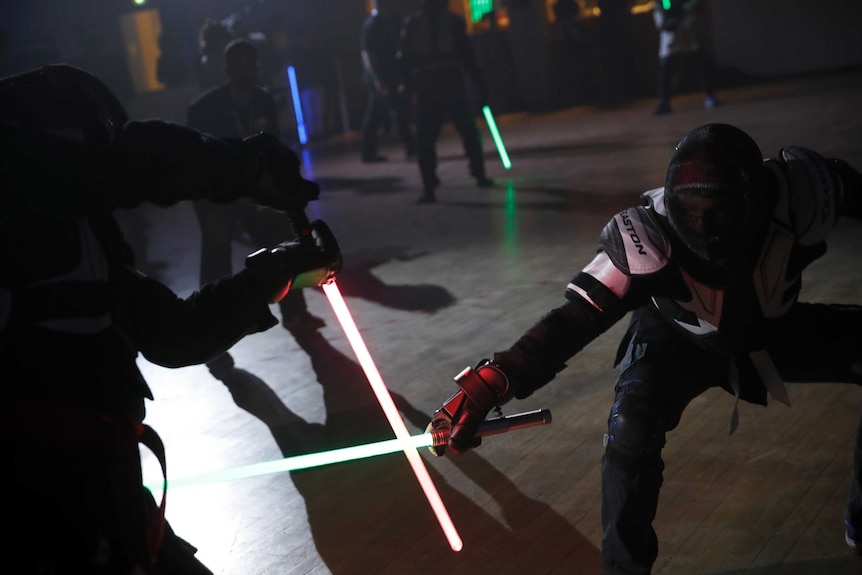 Close up of two people holding coloured lightsabers in a clinch during a duel.