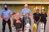 Two police officers smiling with five children at a skate park.