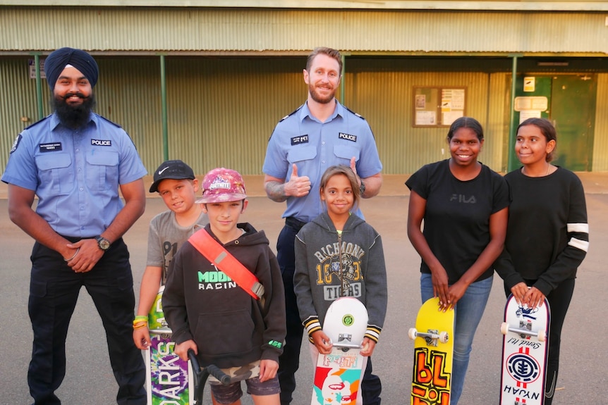 Two police officers smiling with five children at a skate park.