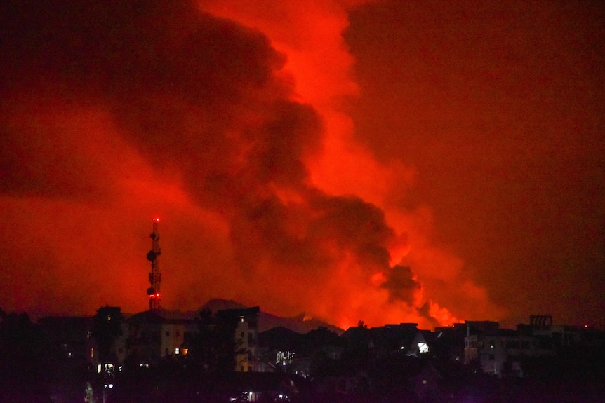 Smoke and flames rise from the volcano as the sky truns red over the city.
