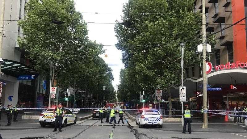 Police tape crosses a street and tram lines on a big city street with trees and tall buildlings on either side