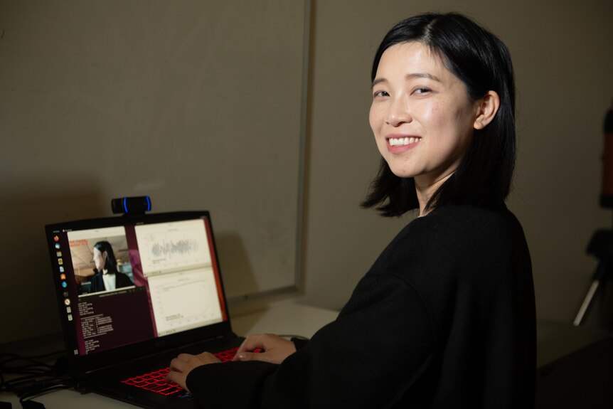 Danyi Wang smiling at the camera, a laptop can be seen in front of her 