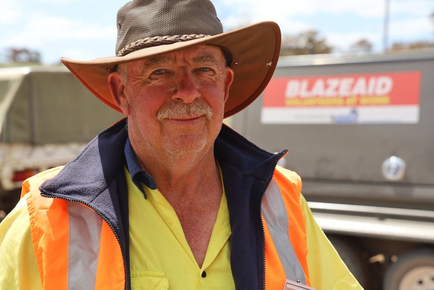 A man in high vis wearing a hat stands in front of a BlazeAid trailer