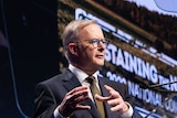 A man in a suit stands at a lectern delivering a speech