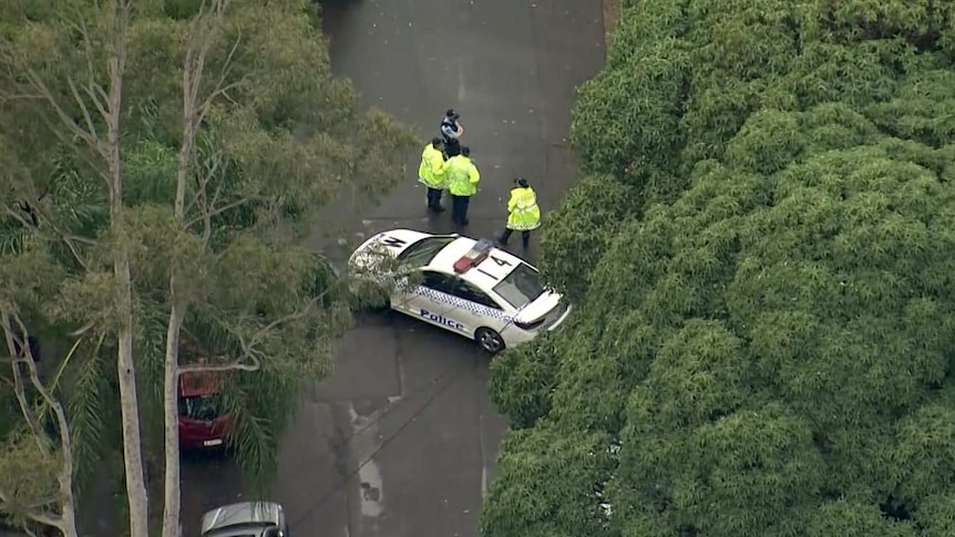 Three police officers stand near a car, which is blocking a car