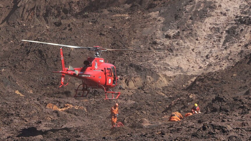 A helicopter hovers over rescue workers searching through muddy sludge