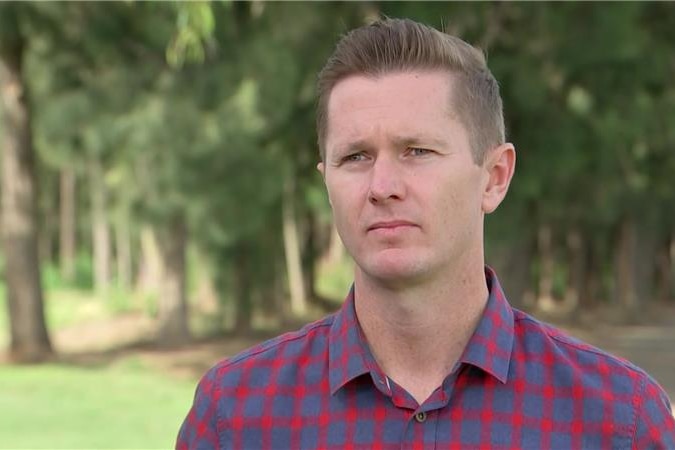 Image of a man wearing a blue and red checked shirt looking to the left of the camera with a serious expression.