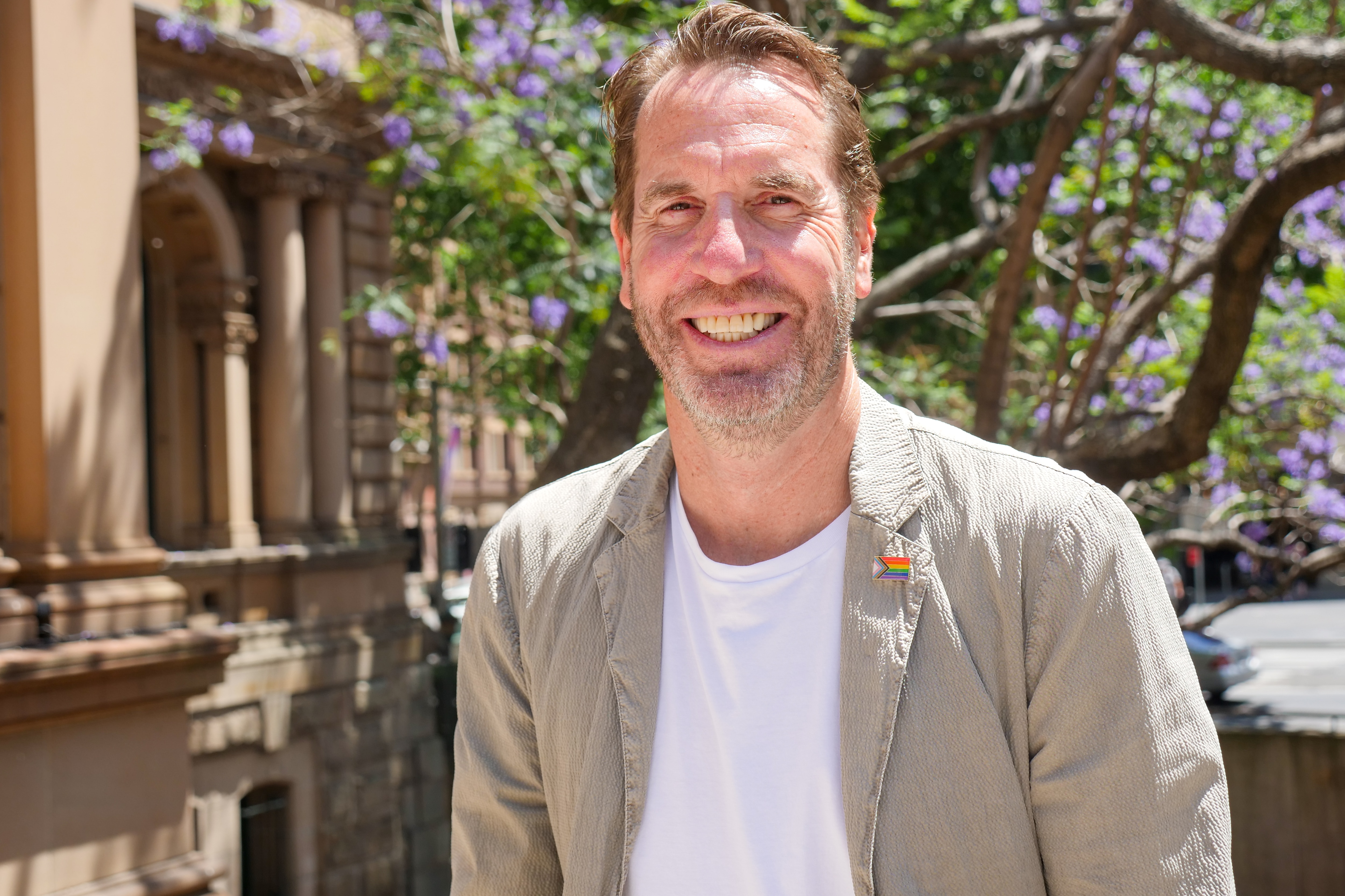 A middle aged man wearing a white t-shirt and beige jacket
