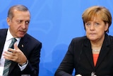 Tayyip Erdogan leans across to speak to a grim faced Angela Merkel.