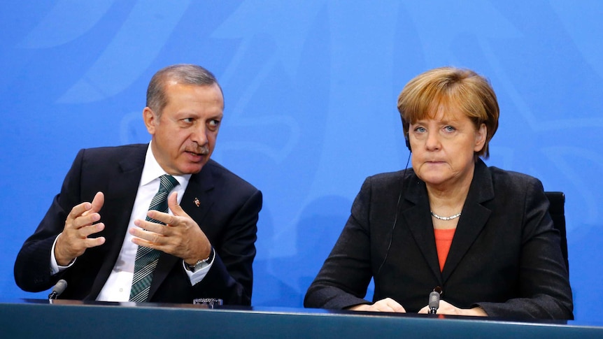 Tayyip Erdogan leans across to speak to a grim faced Angela Merkel.
