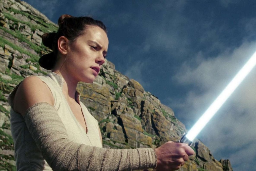 Rey holds a lightsaber in Star Wars The Last Jedi.