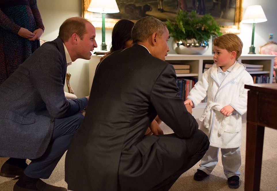 Barack Obama and Prince William crouch down to talk to Prince George who wears a robe