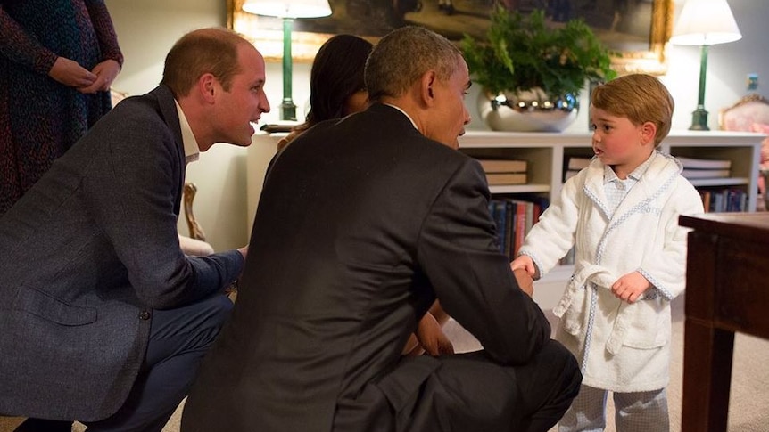 Barack Obama and Prince William crouch down to talk to Prince George who wears a robe
