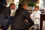 Barack Obama and Prince William crouch down to talk to Prince George who wears a robe