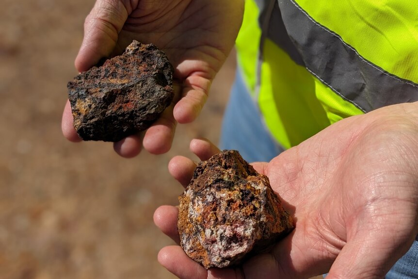 Hands hold rock samples from QMines field investigations.