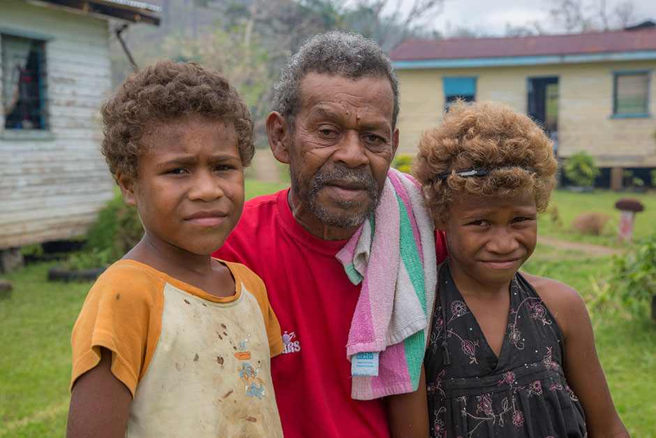 A man stands with his two grandchildren in front of damaged homes