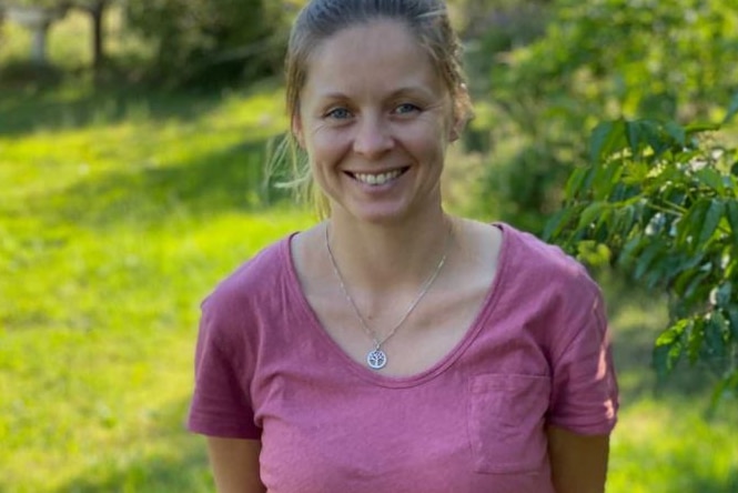 A blonde woman smiles at the camera in a garden.