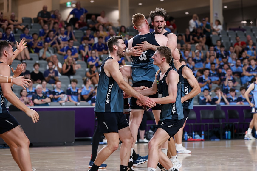 Players wearing dark blue shirts and shorts run together and jump on each other as they celebrate