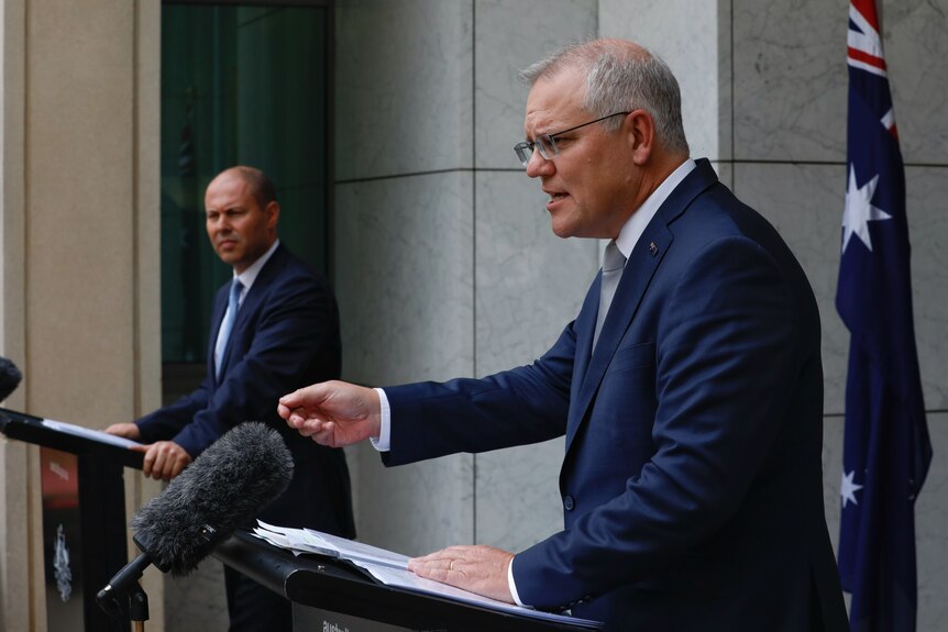Scott Morrison  gestures as he speaks at a lecturn during a media briefing, as Josh Frydenberg looks on