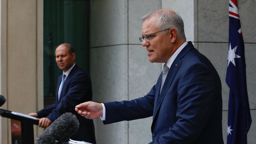 Scott Morrison  gestures as he speaks at a lecturn during a media briefing, as Josh Frydenberg looks on