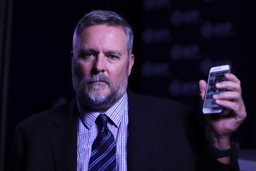 An AFP officer wearing a suit holds up an iPhone.