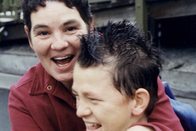 A woman with short dark hair, smiling and holding her son.