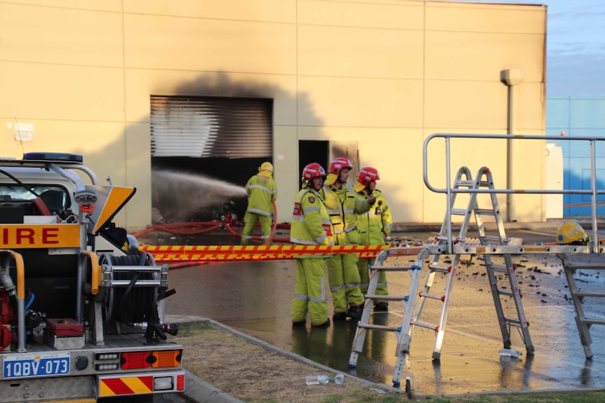Firefighters stand in the foreground while another one aims a hose at a fire in a Bentley shopping centre